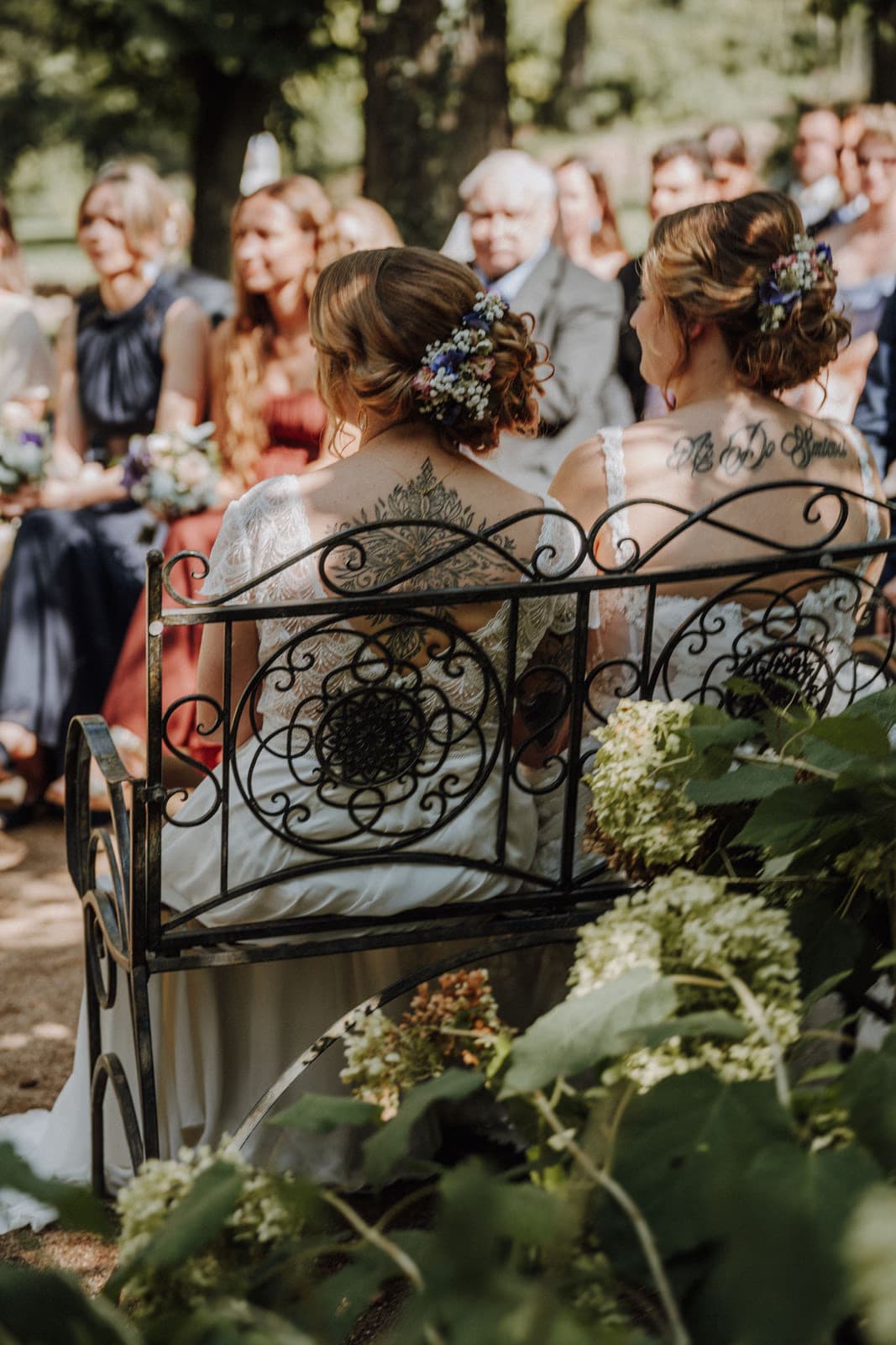 Paar unter dem Traubogen bei der freien Trauung in der Heidelberger Ecke der Villa Renting Eisenberg Pfalz — Rednerin spricht, Gäste auf Holzbänken zwischen Hortensien