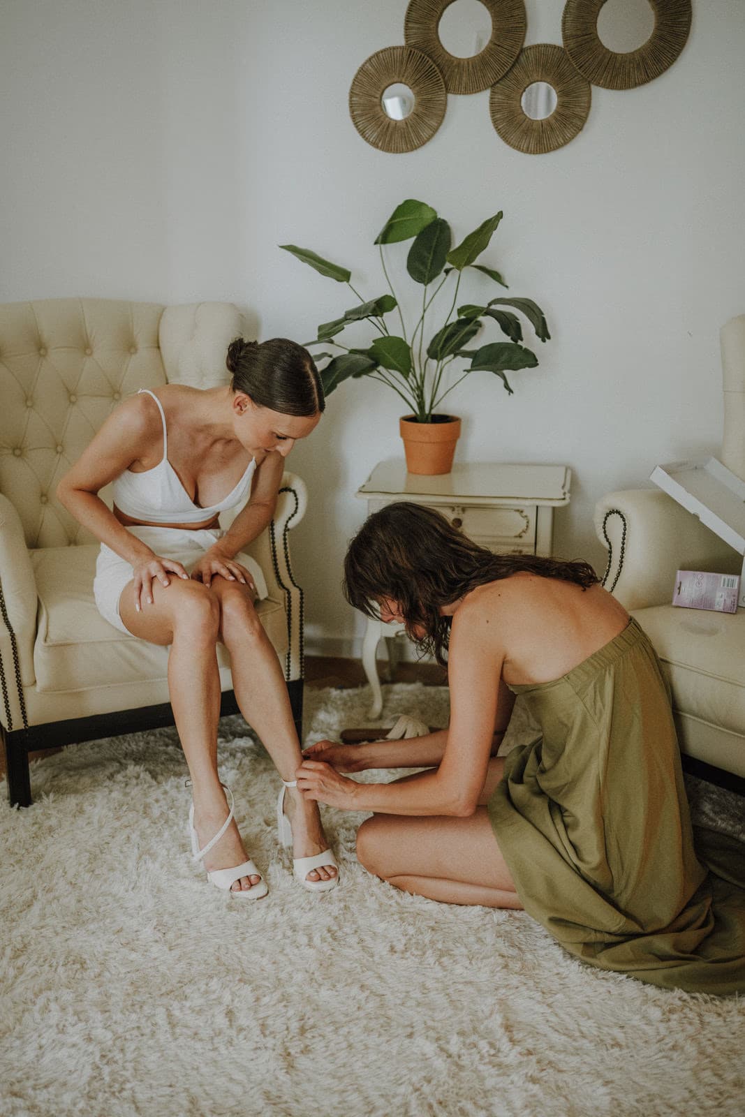 Braut im Sessel beim Getting Ready — Helferin legt Brautschuhe an, Hochzeitssuite Villa Renting Eisenberg Pfalz