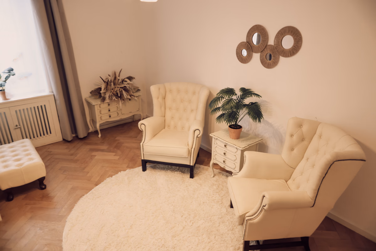 Wohnbereich der Hochzeitssuite mit Ohrensessel, Hocker und rundem Teppich auf Parkettboden, Villa Renting Eisenberg Pfalz